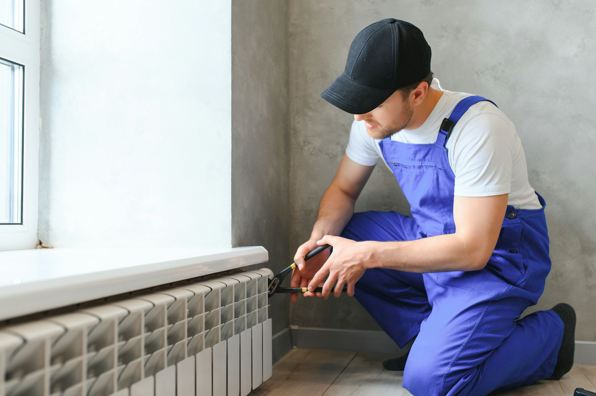 young man plumber checking radiator while installing heating system in apartment